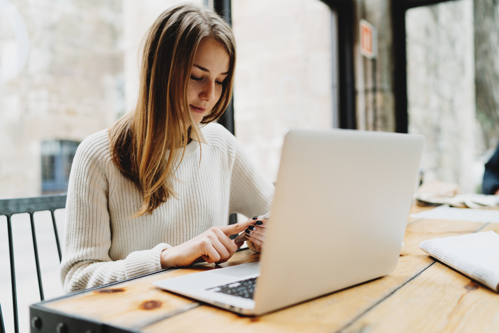 lady on her phone while next to her laptop sitting open